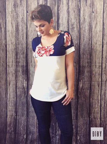 Photo of woman with short hair wearing a color-blocked tee shirt with a pocket. The top shoulder portion and sleeves are a blue floral fabric and the rest is white. 