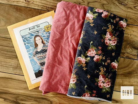 Photo of a table top with a pink fabric and a blue floral fabric with the front of a pdf pattern for a tee shirt dress.