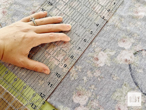 Woman's hand holding clear ruler on wrong side of dark blue floral fabric linking up the straight cutting line.