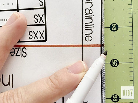 Photo of pattern piece with mark on fold, a brown marker, a ruler, and a woman's hand.