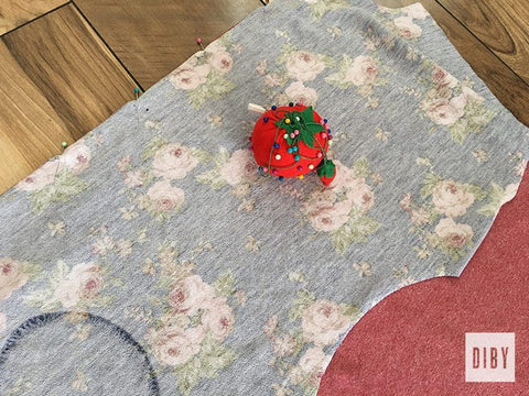 Cut fabric pieces with a pin cushion sitting on it ready to be pinned together. 