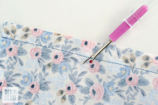 Picture of wrong side of floral fabric with blue stitches and pink seam ripper