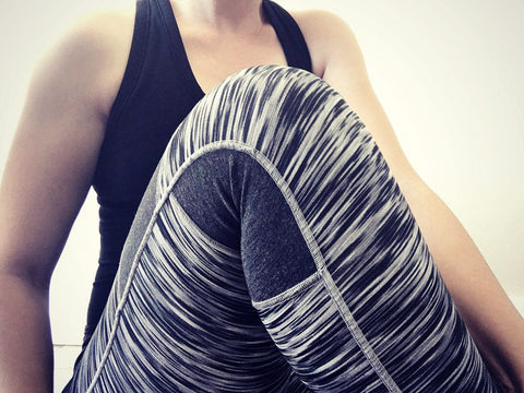 A woman seated wearing a dark tank top and a dark blue and white striped pair of leggings. 