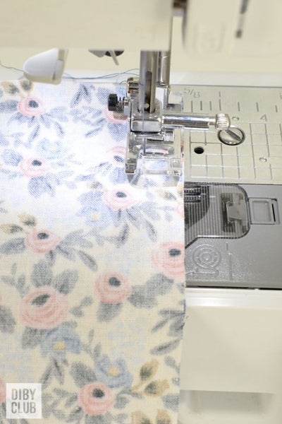 Sewing machine sewing a seam on a piece of floral fabric with wrong side up