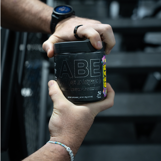 Person holding a container of ABE Ultimate Pre-Workout supplement.