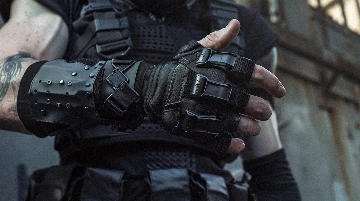 A person is wearing a pair of black, fingerless, tactical gloves featuring reinforced knuckles and adjustable straps.