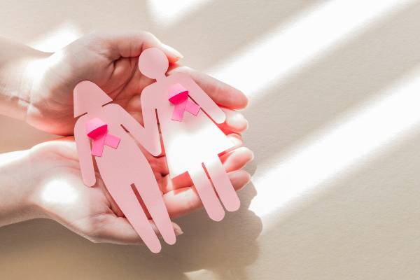 zwei rosa Frauenfiguren aus Papier mit Krebsschleife liegen in zwei Händen