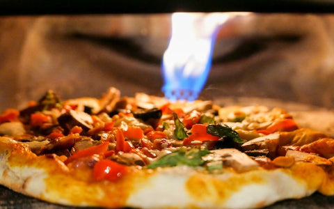 A pizza with vegetables and chicken is being cooked in an oven, with a blue flame visible in the background.