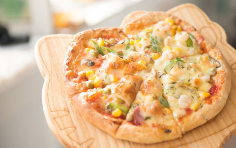 A freshly baked pizza with melted cheese, veggies, and herbs sits on a wooden board.