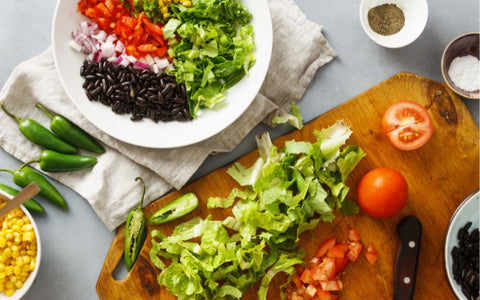 Ingredients for a salad arranged separately on a plate with bowls of corn and tomatoes on the side.