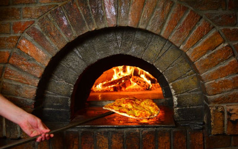A person is taking a pizza out of a brick oven.
