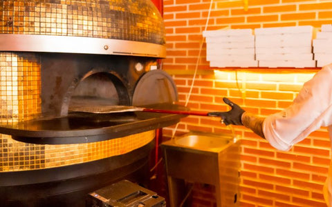 A person putting a stick into a pizza oven.