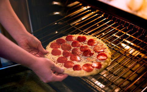 Putting a pepperoni pizza into the oven.