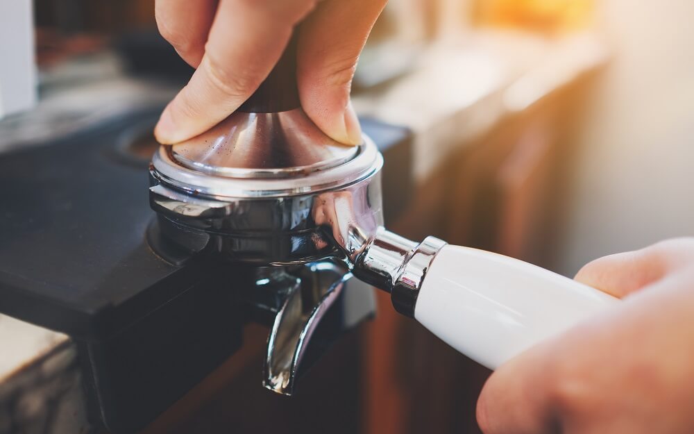 A barista is using a tamper to press coffee grounds