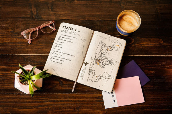 Open travel journal with a world map and checklist, accompanied by a coffee cup, symbolizing the planning phase of travel for a journey documentation article.