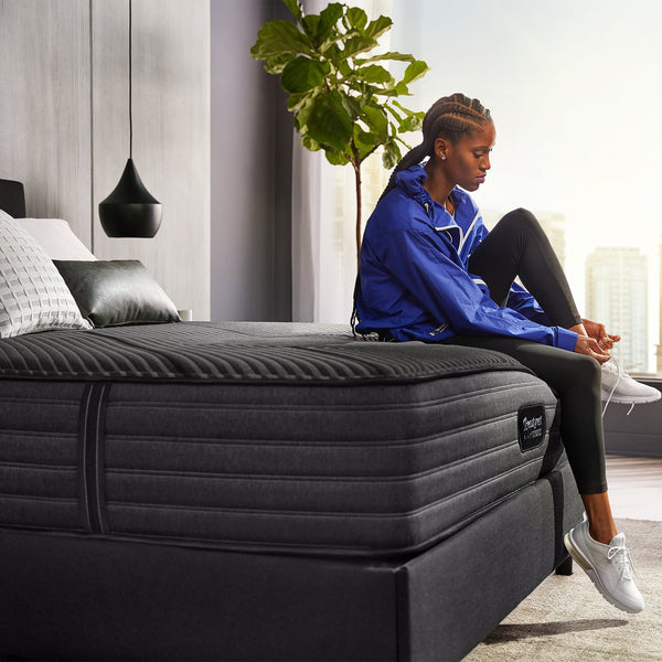 Woman In Sportswear Tying Shoes And Sitting On The Edge Of A Beautyrest Black Hybrid L-Class Firm Mattress