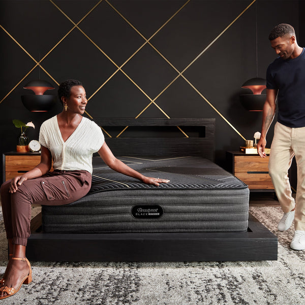 Woman Relaxing On A Beautyrest Black Hybrid K-Class Plush Mattress As A Man Stands Looking At The Mattress