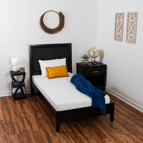 Comfort Essentials Basic Mattress on bed frame in bedroom covered with a yellow throw pillow and a blue throw blanket with small end tables next to