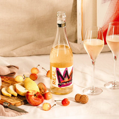 Open bottle of REAL Royal Flush Sparkling Tea next to a selection of fruits.