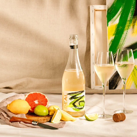 Open bottle of REAL Dry Dragon Sparkling Tea next to a selection of sliced fruits.