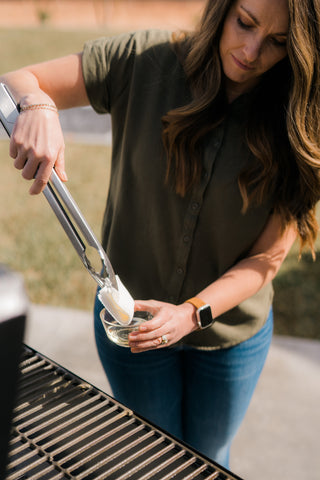 Susie from Hey Grill Hey uses a long set of tongs to dip a folded paper towel in oil as she gets ready to season the grill grate