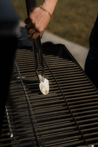 Susie from Hey Grill Hey uses a long set of tongs holding a folded paper towel dipped in oil to season the grill grate