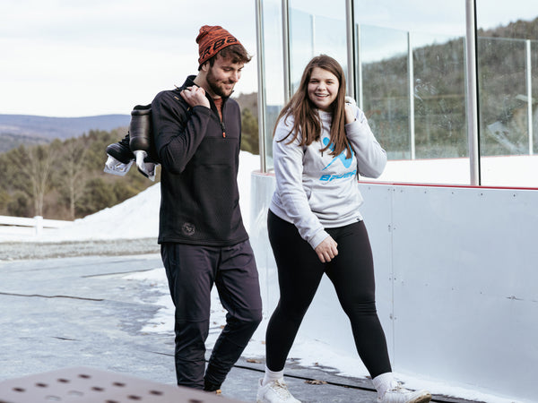 man and woman walking by outdoor ice rink with bauer lifestyle skates over shoulder