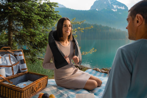 woman sitting on blanket in woods enjoying relaxing massage with cordless massage