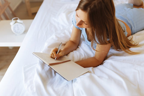 woman lying on bed and taking notes in her journal