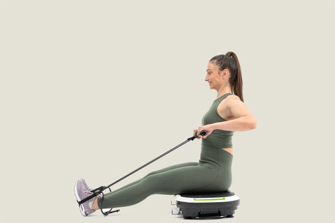 woman doing exercise with resistance bands while sitting on vibration plate