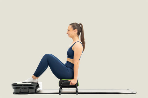 woman doing exercise on vibration plate while sitting on exercise chair