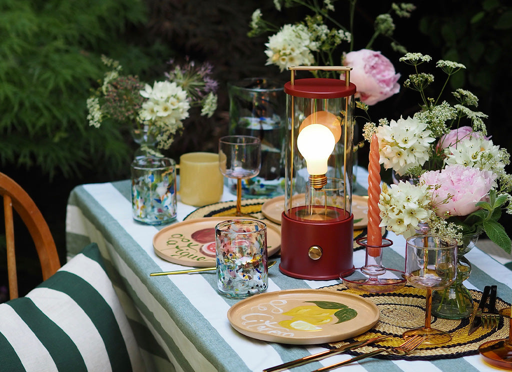 Outdoor dining table prepared for food displaying The Muse Portable Table Lamp in Pomona Red