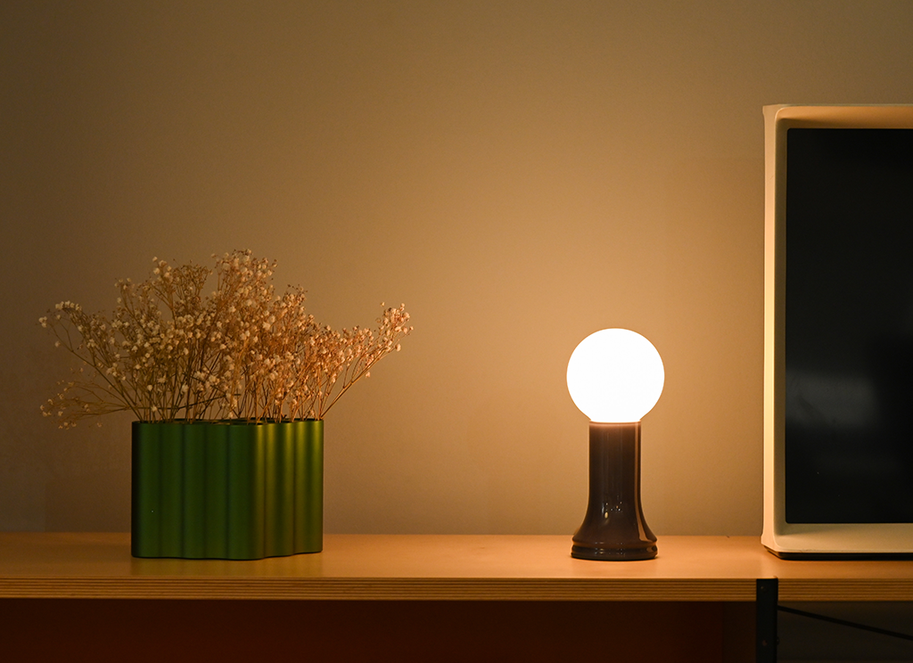 A table surface that displays the Shore table lamp, a green vase and TV