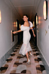 woman walking down hallway in white wedding dress while looking over shoulder behind her