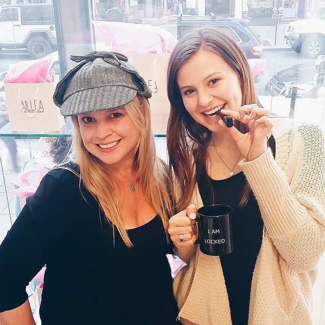 two women posing, one with hat and one with pipe 