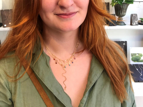 gold rainbow colored bead necklace layered with gold squiggle necklace on gal in green shirt with long red hair