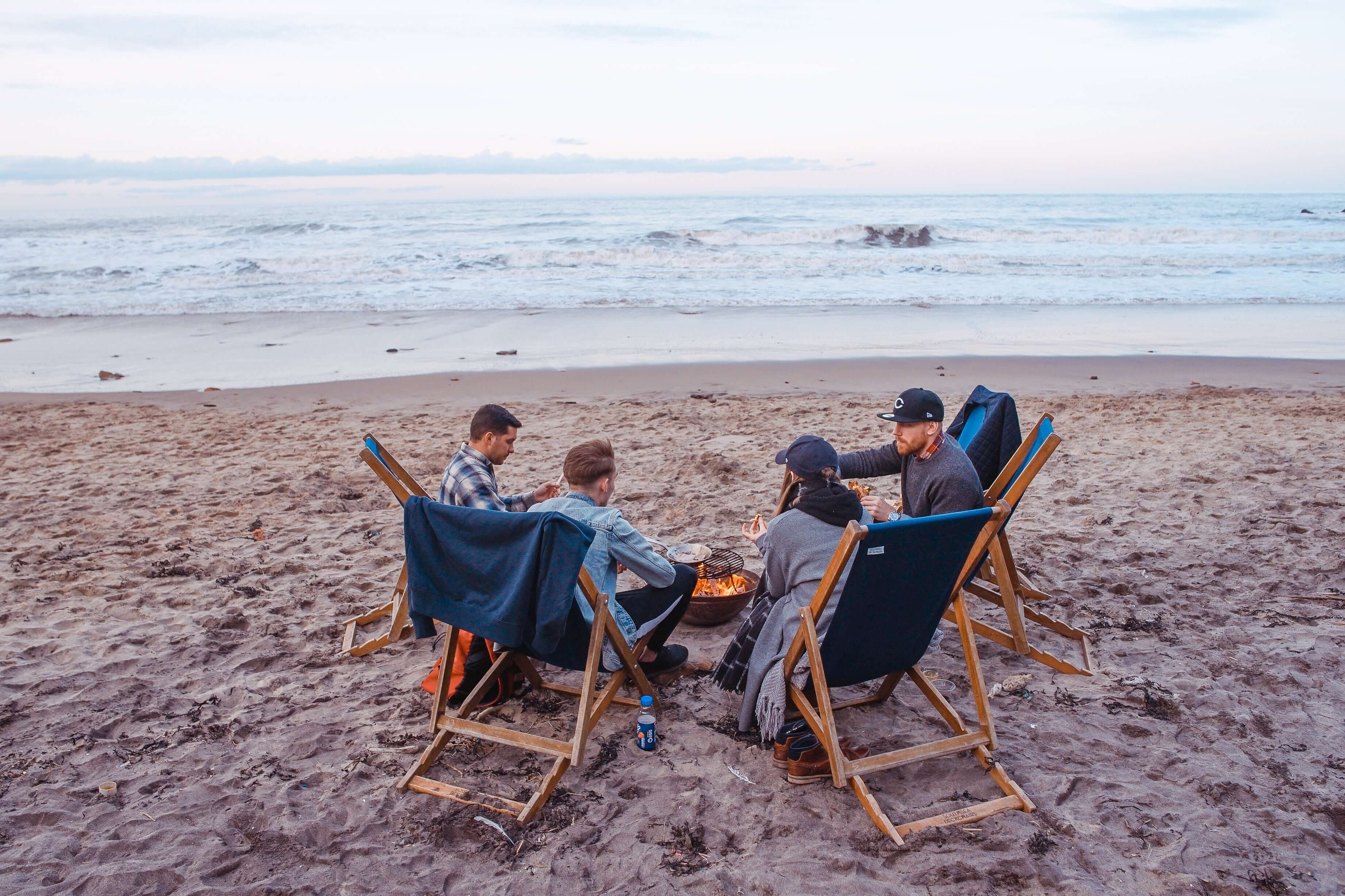 Four friends sitting around a fire at the beach