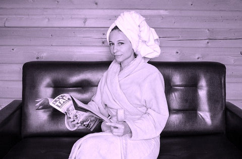 Woman with hair wrapped in towel sitting on couch reading magazine
