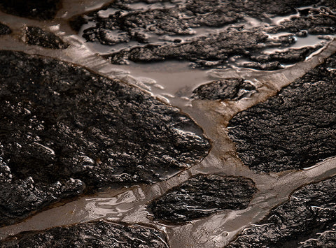 Image of rocks embedded in sand with water running between the spaces between.