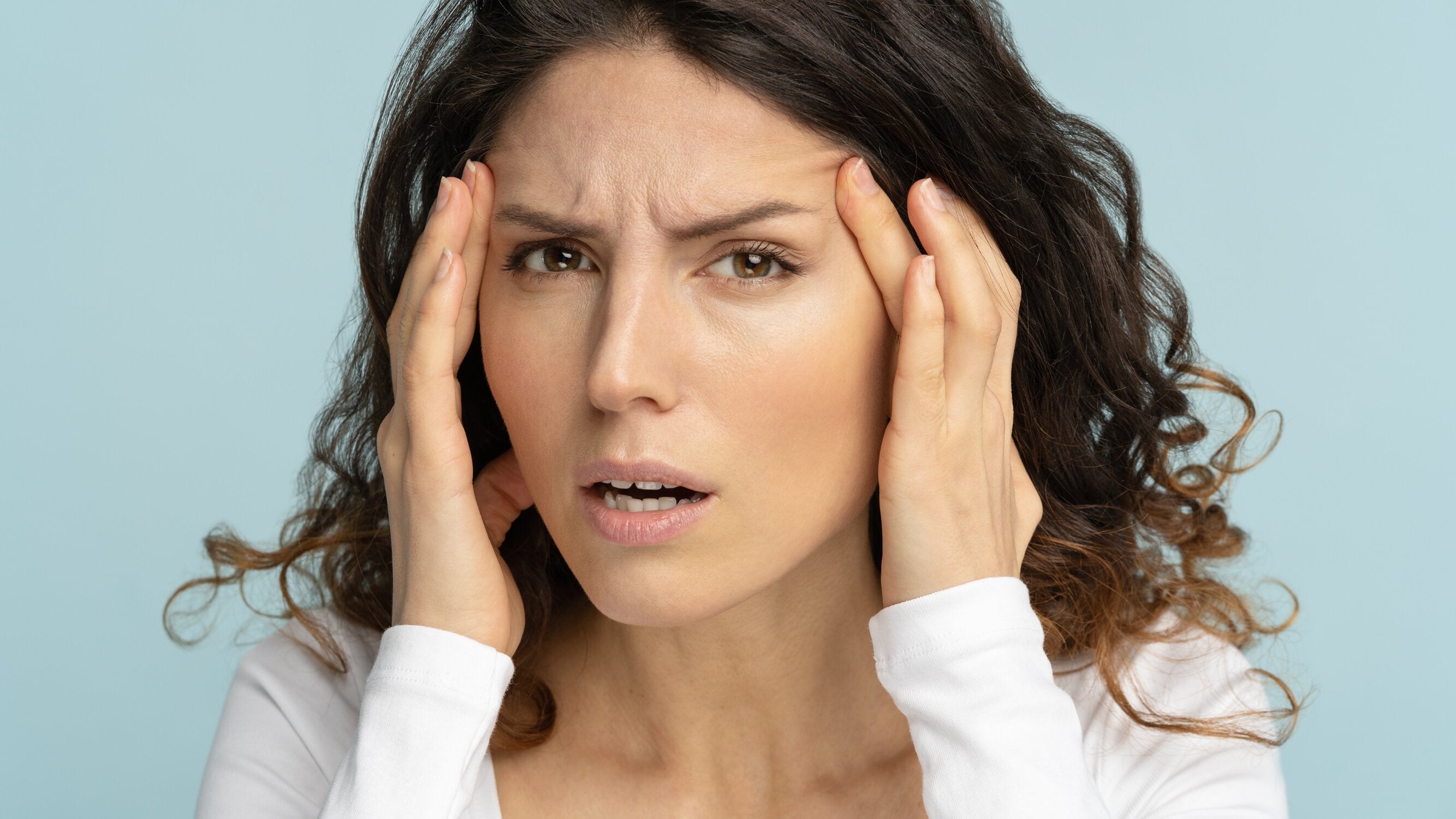 A brunette girl is having a headache, and holding her temple.