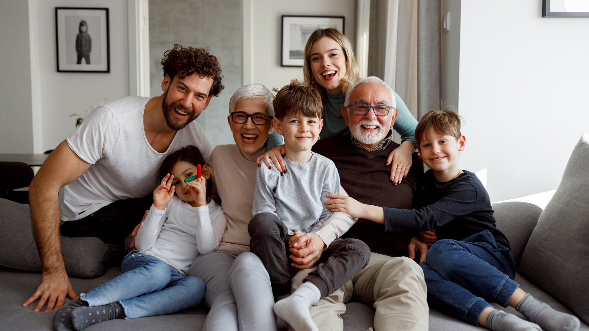 Multigenerational family smiling together on a couch in a cozy living room.