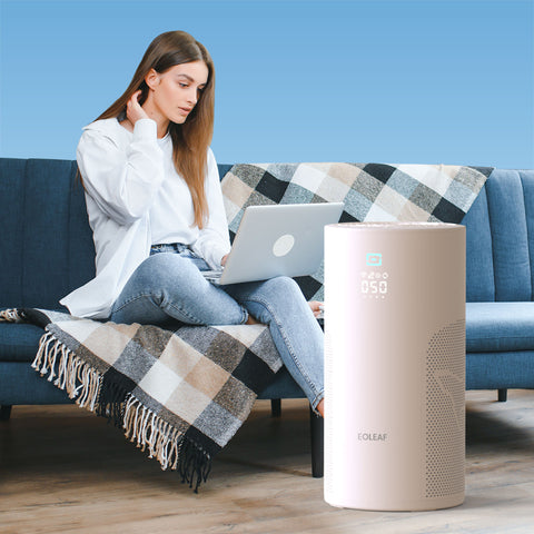 A woman sitting on a blue couch on her laptop next to Eoleaf's AEROPRO 40 air purifier