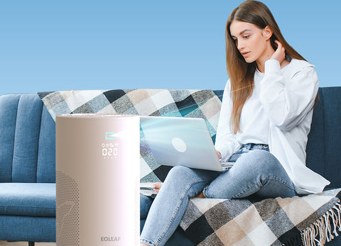 A woman using a laptop on a couch next to Eoleaf's AERO PRO 40 air purifier