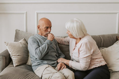 Un vieil homme qui tousse avec une femme âgée qui lui tient la main