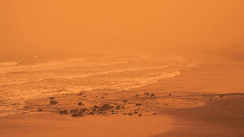 Une plage sous un ciel orange impacté par la poussière du désert du Sahara