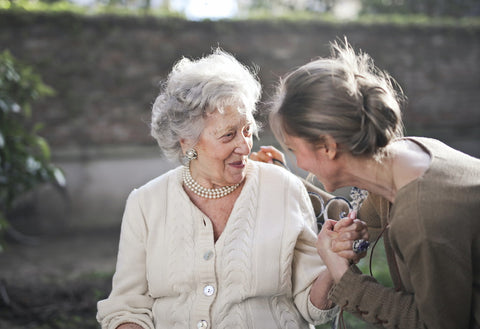An elderly woman holding hands and talking with a younger woman