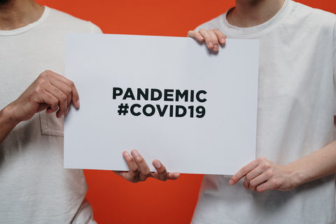 Two people holding a sign that says 'PANDEMIC #COVID19'