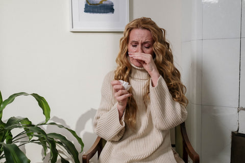 A woman next to a plant blowing her nose into a tissue
