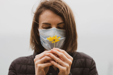 A woman wearing a mask smelling a flower