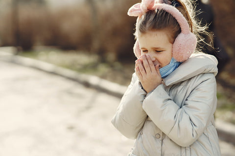 A young girl with pink earmuffs sneezing